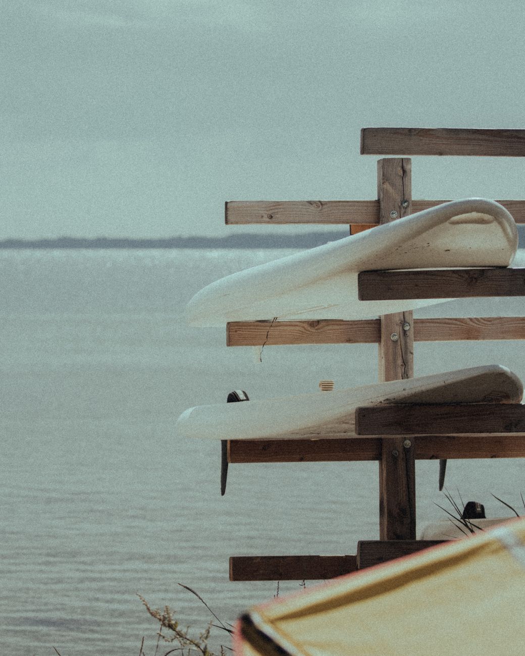Wooden surfboard rack by a calm seaside, perfect for summer vacations.