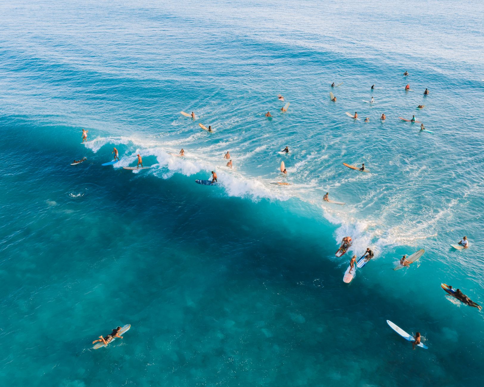 High-angle shot of surfers enjoying a vibrant day riding waves in blue ocean waters.