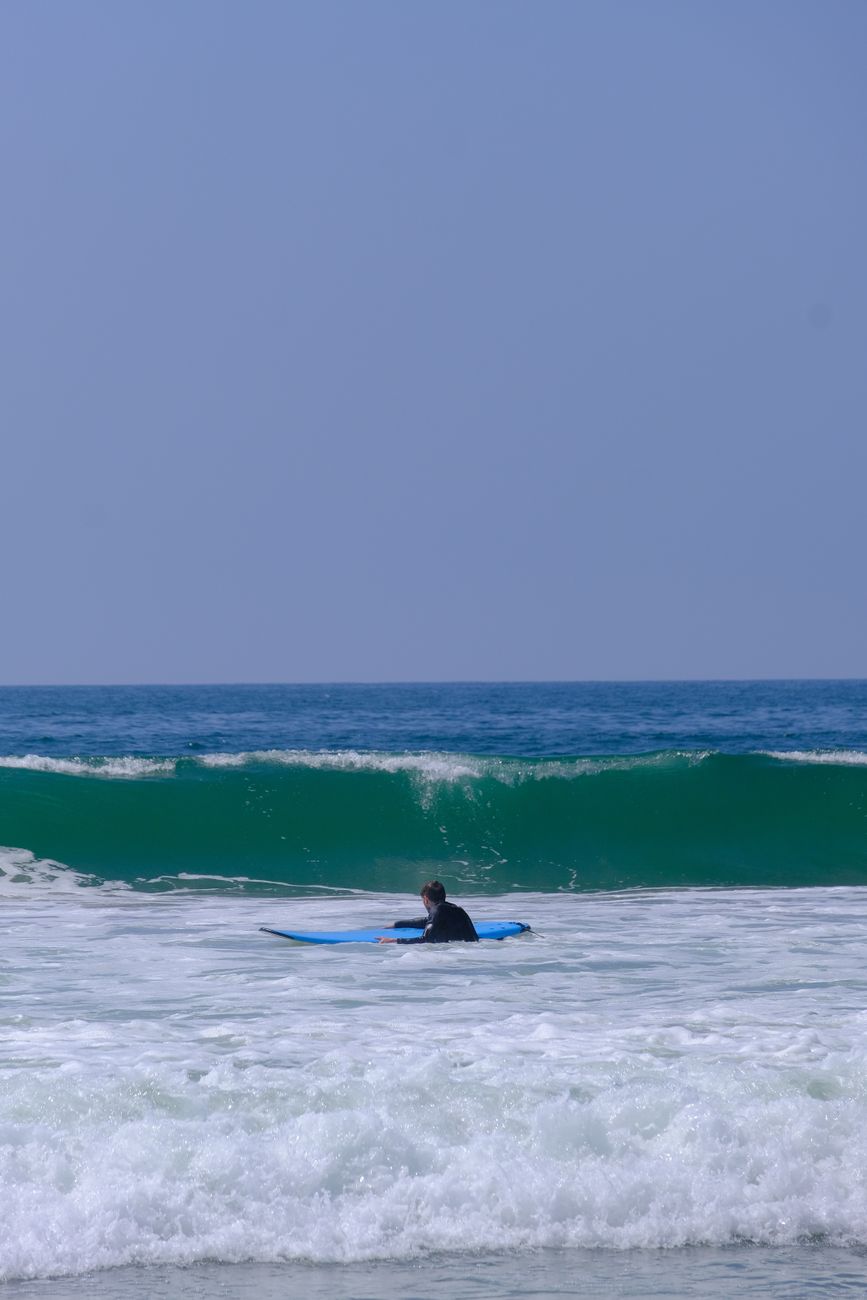 A lone surfer paddles towards the waves on a sunny day at the beach.