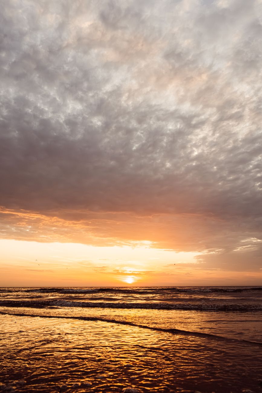 Golden sunset casting a warm glow over Middelkerke beach, Belgium, under dramatic clouds.